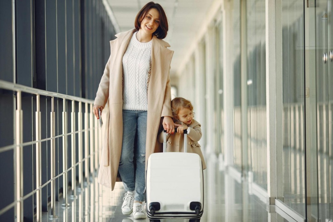 A mom and daughter in an airport walking with a suitcase